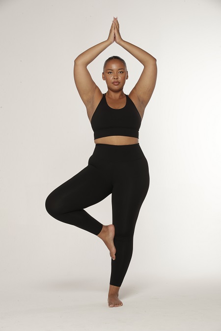 Woman doing yoga tree pose with hands in prayer above head wearing macthing black activewear set.